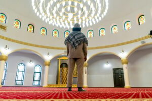 Muslim man stands on carpet in the middle of the prayer hall at the mosque with his head raised up